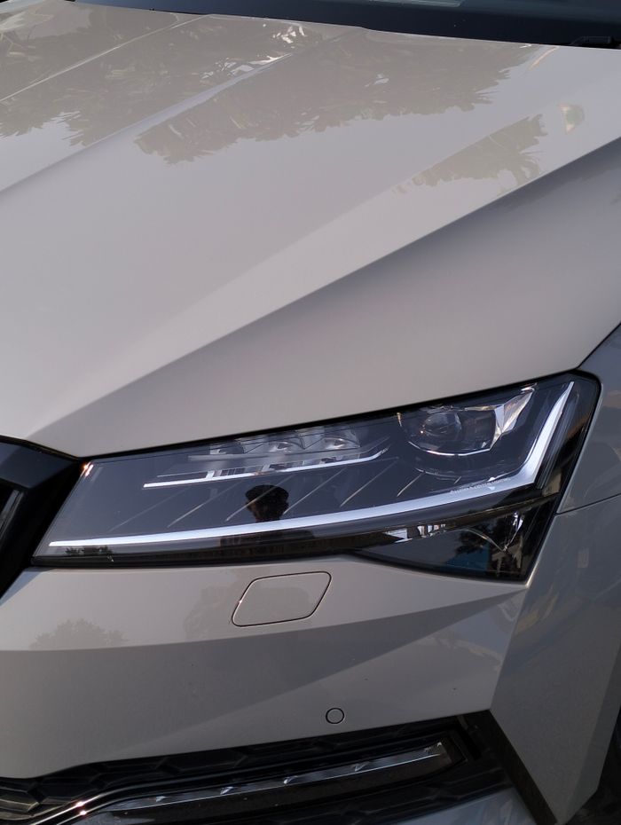 Sleek and modern car headlight and hood close-up with reflective chrome detail.