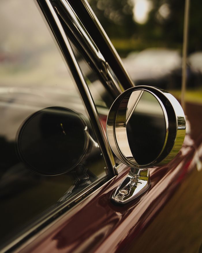 Detailed view of a vintage car's side mirror reflecting surrounding environment.